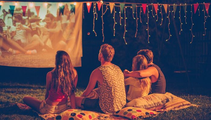 A family sits in the backyard watching a movie on their projector.